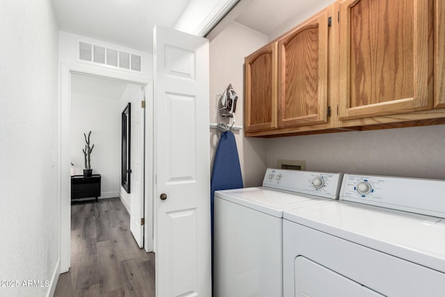 clothes washing area with washer and dryer, cabinet space, wood finished floors, and visible vents