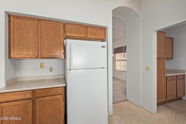 kitchen with freestanding refrigerator, arched walkways, brown cabinetry, and light countertops