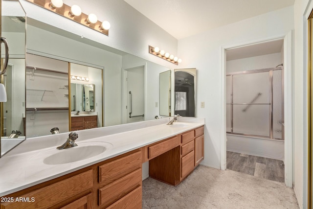 full bath featuring double vanity, a sink, wood finished floors, and bath / shower combo with glass door