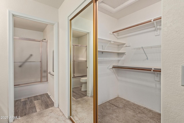 full bath featuring combined bath / shower with glass door, toilet, wood finished floors, and a spacious closet