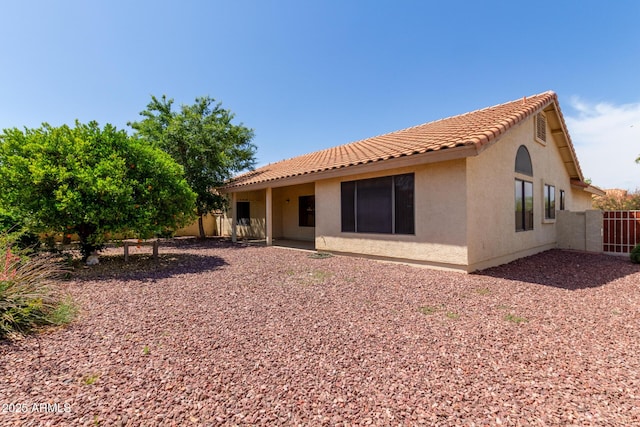 rear view of house featuring fence, stucco siding, and a tile roof