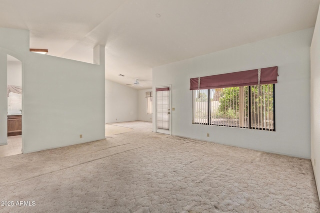 carpeted empty room with arched walkways, ceiling fan, and vaulted ceiling