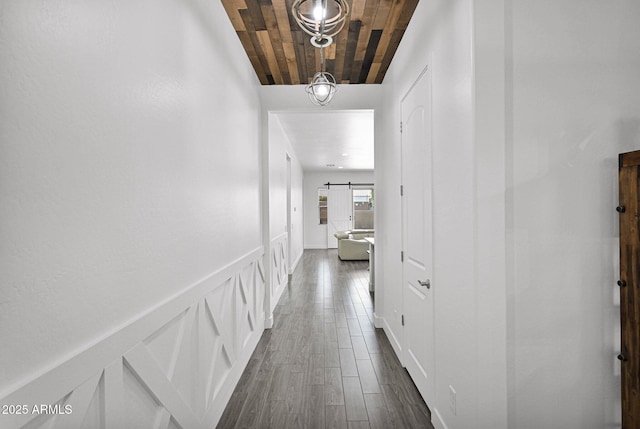 hall with dark wood finished floors, wainscoting, a barn door, a decorative wall, and wooden ceiling