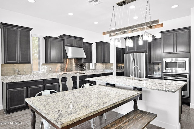 kitchen with a center island with sink, visible vents, a sink, under cabinet range hood, and appliances with stainless steel finishes