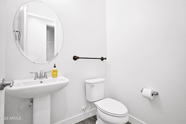 half bathroom featuring toilet, baseboards, and a sink