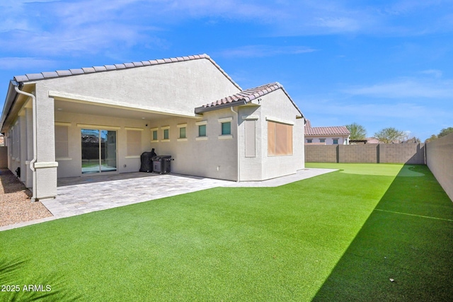 rear view of property with a tiled roof, stucco siding, a fenced backyard, a yard, and a patio