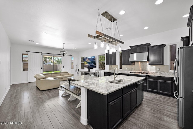 kitchen featuring a sink, under cabinet range hood, a barn door, appliances with stainless steel finishes, and dark cabinets