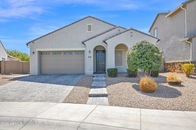 view of front of home featuring fence, a tiled roof, stucco siding, decorative driveway, and a garage