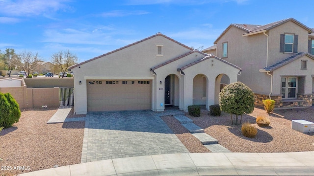 mediterranean / spanish home with fence, a tiled roof, stucco siding, decorative driveway, and an attached garage