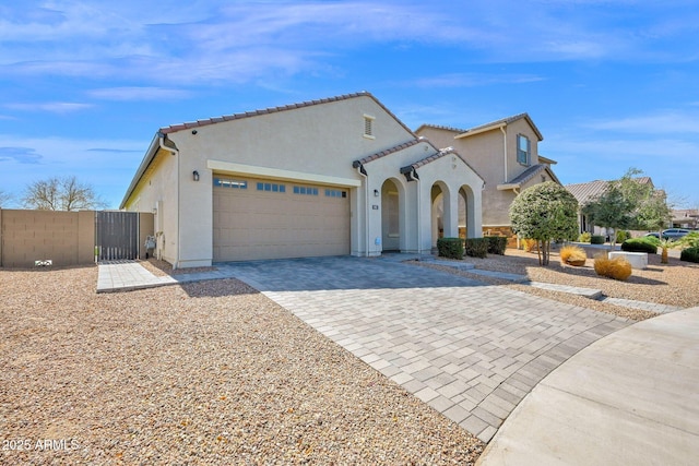 mediterranean / spanish house featuring a gate, stucco siding, a garage, a tile roof, and decorative driveway