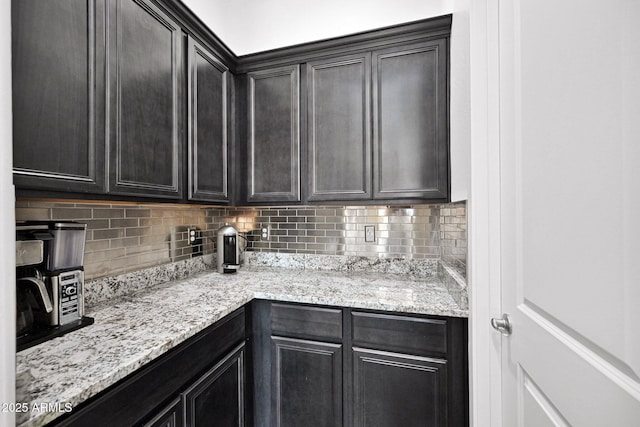 kitchen featuring light stone countertops, backsplash, and dark cabinetry