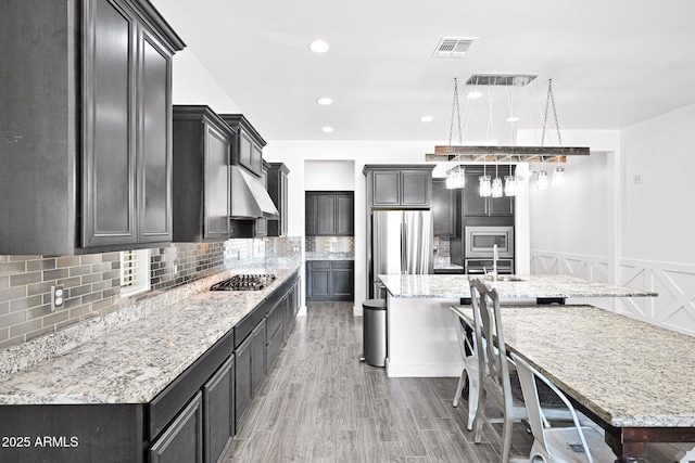 kitchen with tasteful backsplash, visible vents, light stone countertops, a large island with sink, and appliances with stainless steel finishes