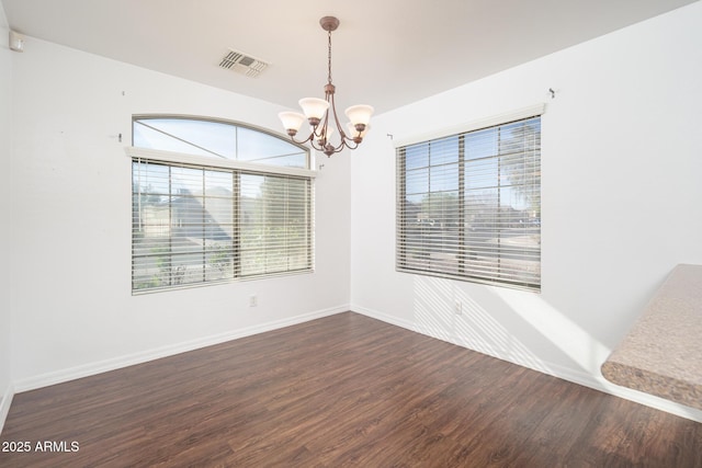 empty room featuring visible vents, baseboards, an inviting chandelier, and wood finished floors