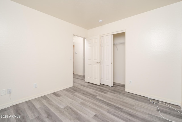 unfurnished bedroom featuring wood finished floors, a closet, and baseboards