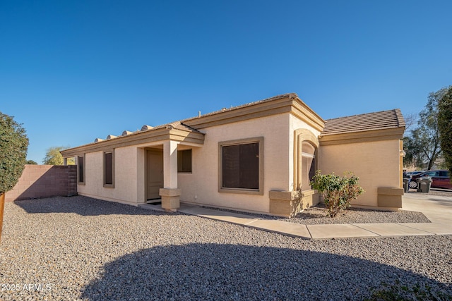 back of property with stucco siding, a tiled roof, and fence