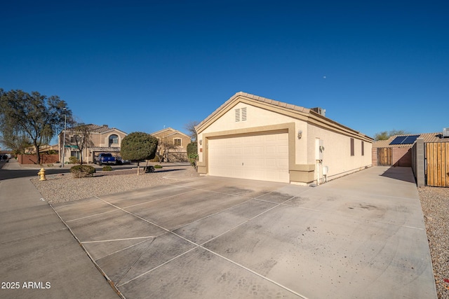 view of side of property featuring fence, stucco siding, a garage, driveway, and a gate