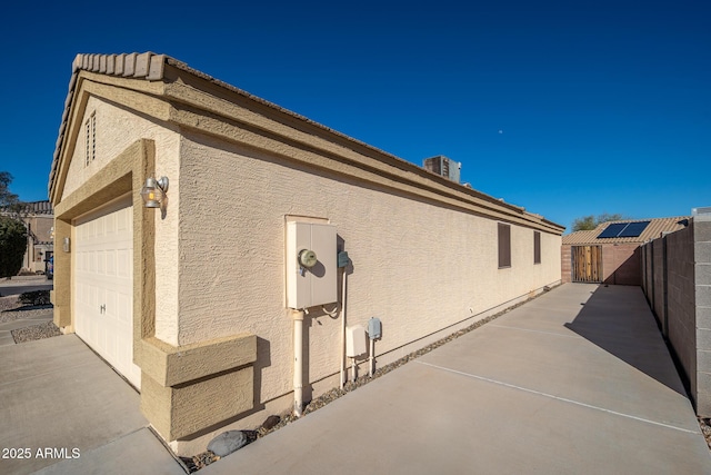 view of home's exterior with an attached garage, fence, and stucco siding