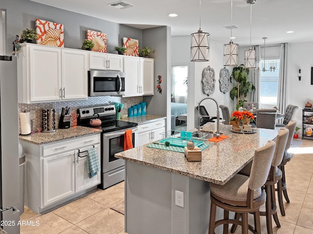 kitchen with white cabinetry, a kitchen island with sink, hanging light fixtures, and appliances with stainless steel finishes