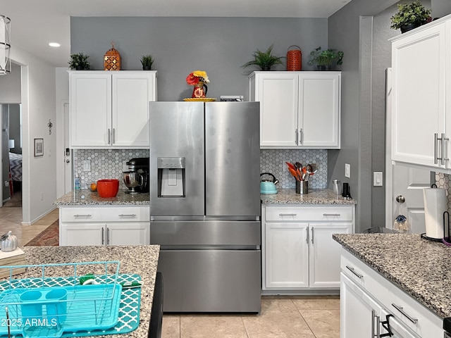 kitchen featuring backsplash, stone counters, stainless steel fridge, and white cabinetry