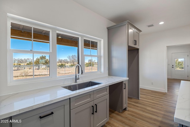 kitchen with light stone counters, sink, and gray cabinets