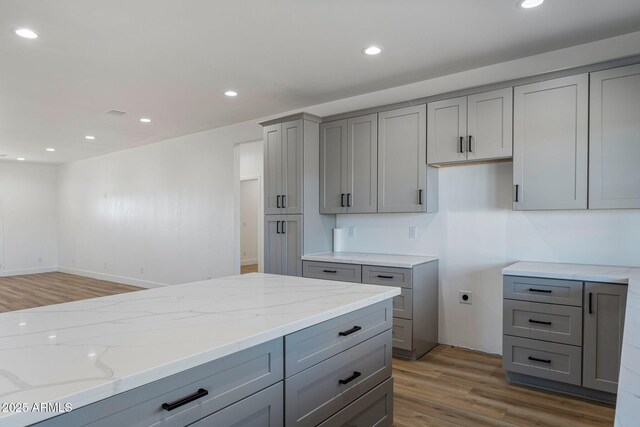 kitchen with gray cabinets, hardwood / wood-style floors, and light stone countertops