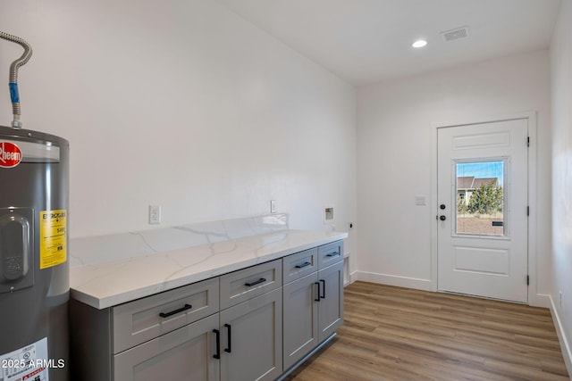 interior space with gray cabinets, light stone countertops, electric water heater, and light hardwood / wood-style floors