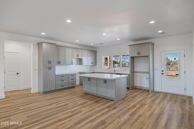 kitchen with gray cabinets, a kitchen island, sink, and light hardwood / wood-style floors