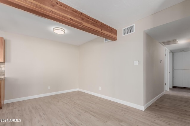 empty room with beam ceiling and light hardwood / wood-style flooring