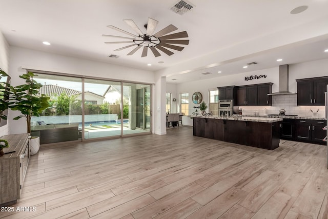 2316 E Canary Dr, Gilbert, AZ 85297 - kitchen featuring wall chimney range hood, open floor plan, light wood finished floors, light stone countertops, and stainless steel appliances