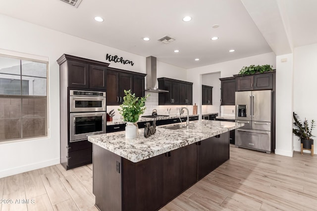 2316 E Canary Dr, Gilbert, AZ 85297 - kitchen featuring appliances with stainless steel finishes, wall chimney range hood, a sink, decorative backsplash, and a kitchen island with sink