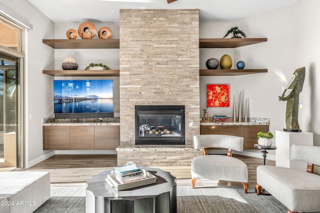 living room with light hardwood / wood-style floors, built in features, and a stone fireplace