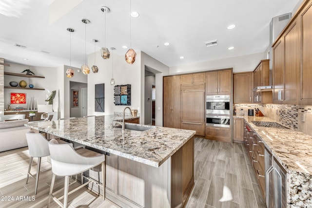 kitchen with light stone countertops, tasteful backsplash, sink, decorative light fixtures, and a large island