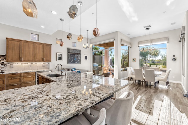 kitchen featuring pendant lighting, sink, decorative backsplash, light stone counters, and a breakfast bar area