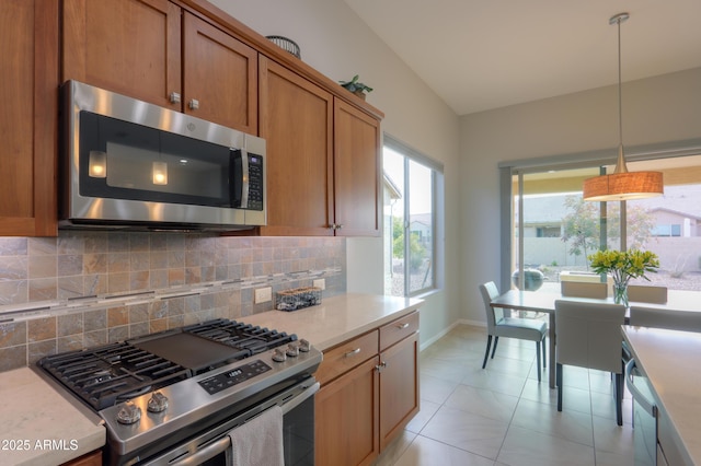 kitchen with appliances with stainless steel finishes, lofted ceiling, decorative light fixtures, tasteful backsplash, and light tile patterned floors