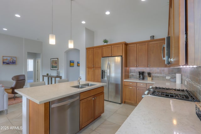 kitchen with an island with sink, appliances with stainless steel finishes, decorative backsplash, light stone countertops, and sink