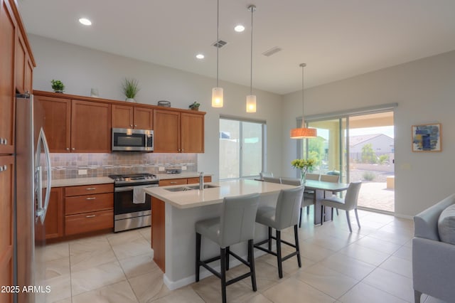 kitchen featuring a kitchen bar, an island with sink, appliances with stainless steel finishes, backsplash, and hanging light fixtures