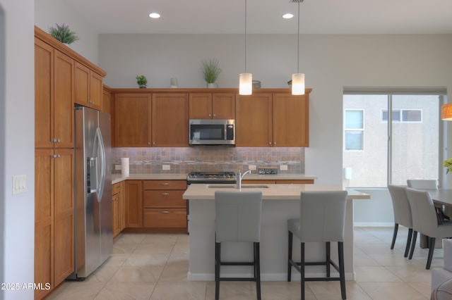 kitchen featuring decorative light fixtures, tasteful backsplash, a center island with sink, appliances with stainless steel finishes, and a kitchen breakfast bar