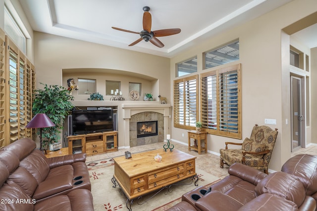 living room featuring light tile patterned flooring, ceiling fan, a tile fireplace, and a raised ceiling