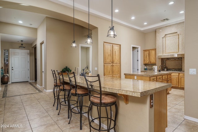 kitchen featuring tasteful backsplash, decorative light fixtures, a large island, light tile patterned floors, and a breakfast bar area