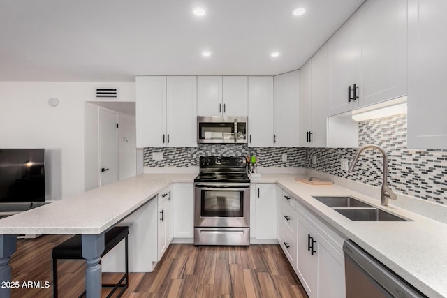 kitchen with stainless steel appliances, dark wood-type flooring, a peninsula, a sink, and white cabinets