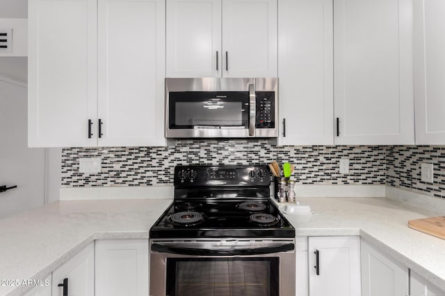 kitchen featuring appliances with stainless steel finishes, light stone countertops, white cabinetry, and decorative backsplash