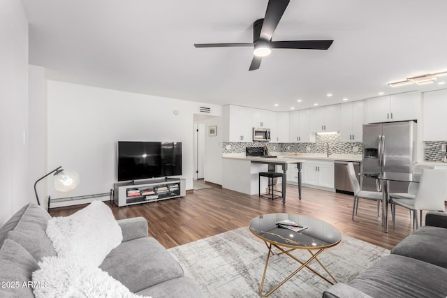 living room featuring a ceiling fan, visible vents, baseboard heating, and wood finished floors