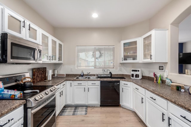 kitchen with appliances with stainless steel finishes, sink, dark stone countertops, white cabinets, and light hardwood / wood-style flooring