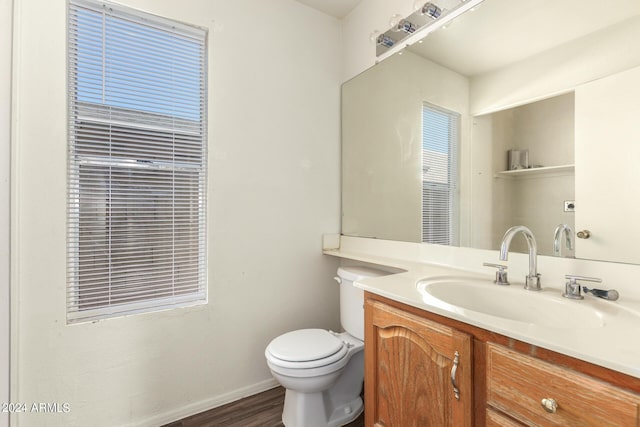 half bath with toilet, wood finished floors, vanity, and baseboards