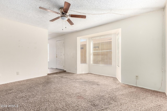 carpeted spare room featuring baseboards, a ceiling fan, and a textured ceiling