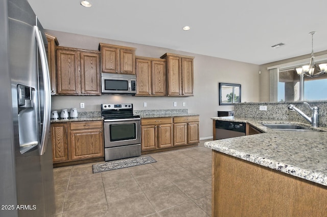 kitchen with sink, decorative light fixtures, light stone countertops, appliances with stainless steel finishes, and a notable chandelier