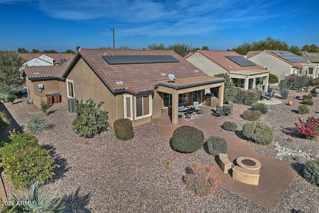 back of house with central AC unit, solar panels, a patio area, and an outdoor living space with a fire pit