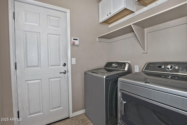 clothes washing area with cabinets, light tile patterned floors, and washer and clothes dryer