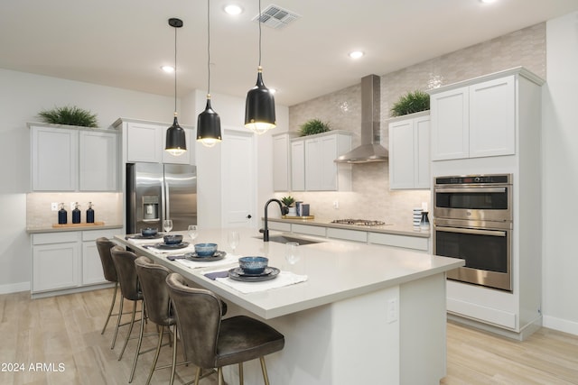 kitchen with wall chimney exhaust hood, visible vents, appliances with stainless steel finishes, a sink, and light wood finished floors