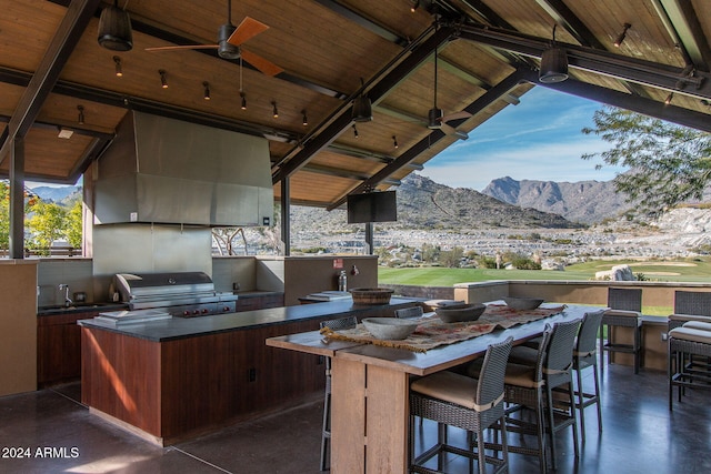 view of patio featuring area for grilling, a wet bar, ceiling fan, a mountain view, and a grill